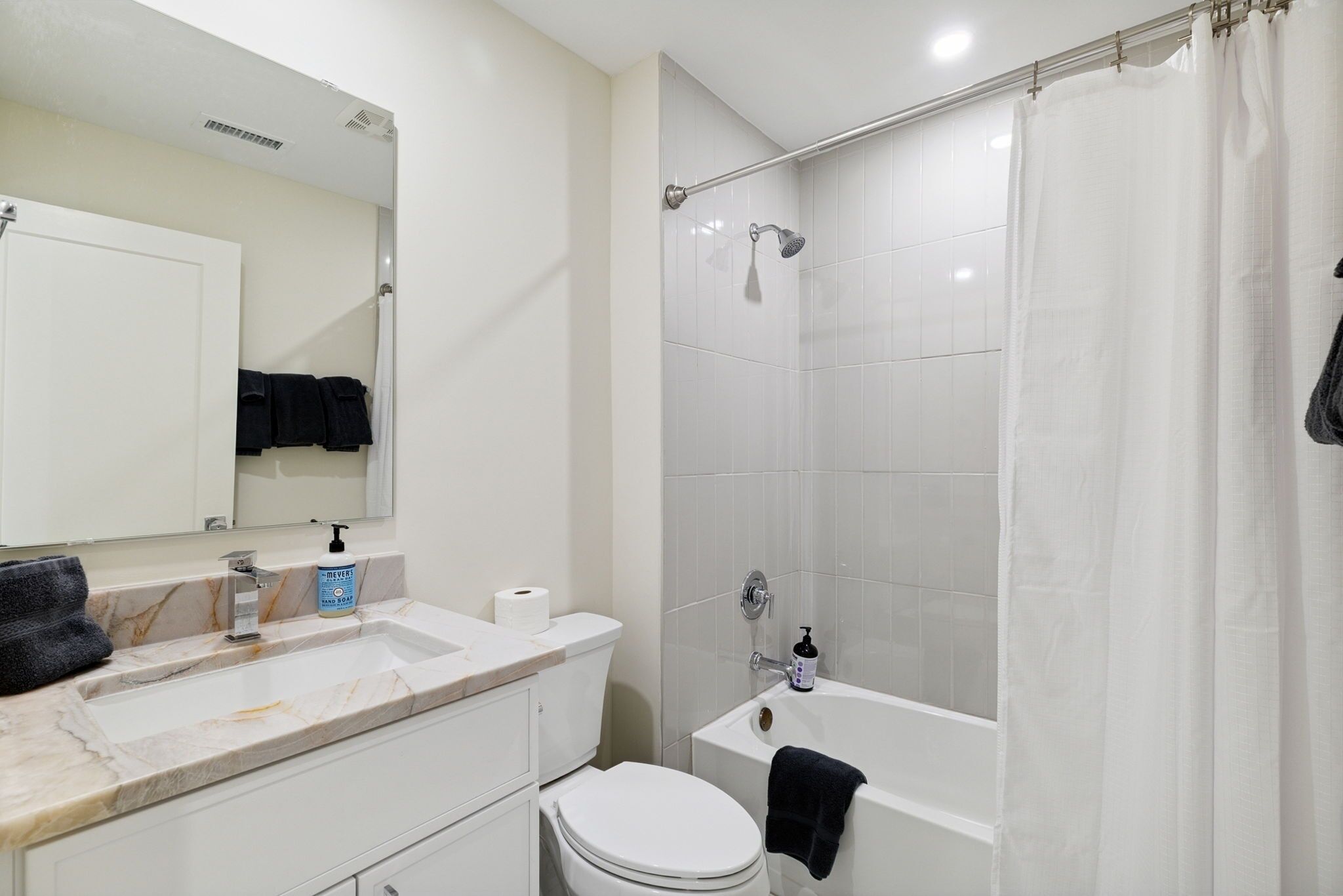 Une salle de bain avec des toilettes blanches, un lavabo doté d’un plan de travail en marbre, une baignoire et un rideau de douche.