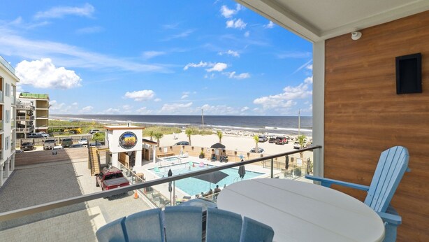 A balcony with a view of the beach, a pool, and a building with a sign.