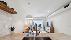 A modern kitchen with a marble countertop, stainless steel sink, and a ceiling fan.