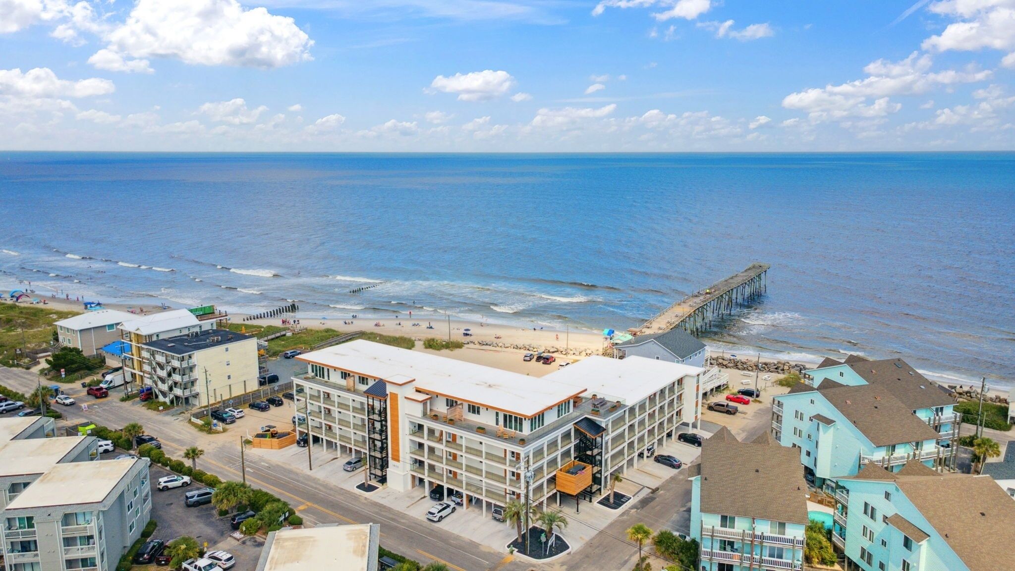 Um hotel à beira-mar, com vários andares, estacionamento e vista para a praia e oceano.