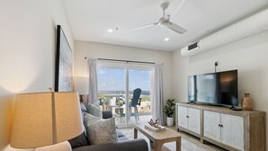 A modern living room with a sofa, a coffee table, a TV on a wooden cabinet, and a ceiling fan.