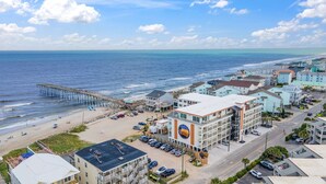 A coastal town with a pier extending into the ocean, beachfront buildings, and a parking area.