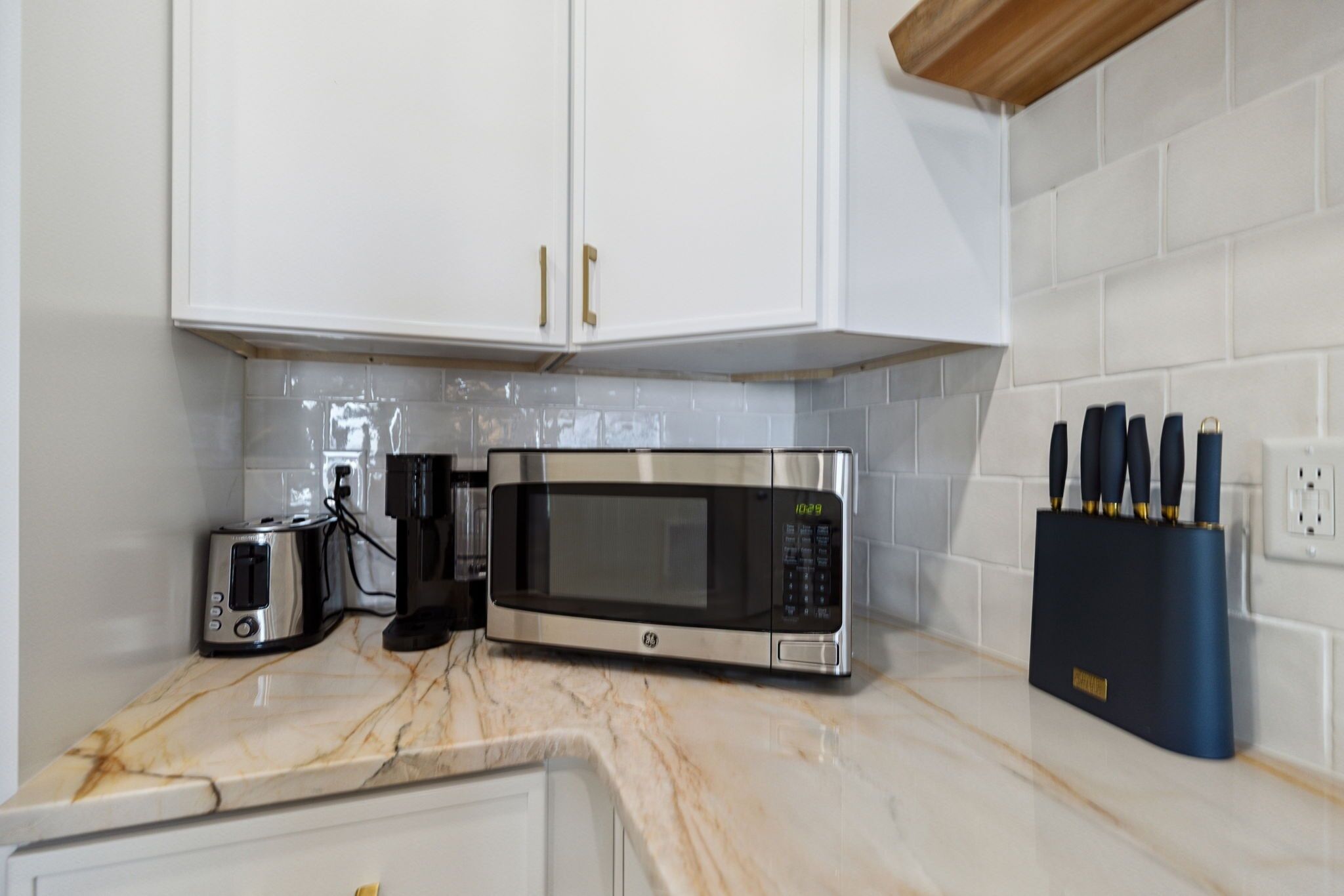 Une cuisine avec des meubles blancs, un four à micro-ondes en acier inoxydable, un grille-pain et un bloc à couteaux.
