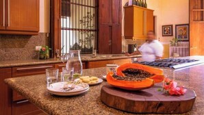 A kitchen with granite countertops, wooden cabinets, and a large window with bars. - Luxurious and Private Hacienda near Merida (Fraccionamiento Chuntuak, Molas)