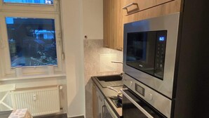 Cocina compacta con microondas, horno y lavaplatos. Se ve una ventana con vistas a un edificio.