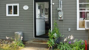 A gray single-story house with a front door, a small window, and a visible electrical box.