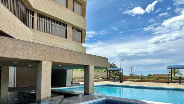 Una piscina con superficie de agua azul cristalina, rodeada por una plataforma de concreto y un edificio con ventanas protegidas por barrotes.
