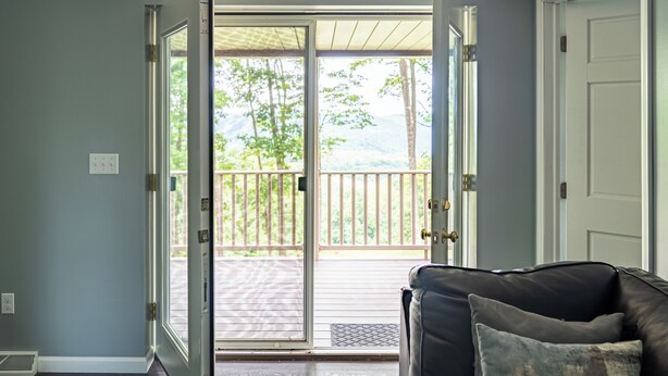 Eine geöffnete Tür, die auf einen Balkon mit Blick auf Bäume und eine Holzterrasse führt.