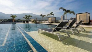 A swimming pool with lounge chairs and palm trees, with mountains in the background. - Luxury Loft Porto Horizonte Beach meters away (Magdalena)