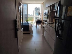 A modern kitchen with a refrigerator, a dining area with a chair, and a bed in the background. - Luxury Loft Porto Horizonte Beach meters away (Magdalena)