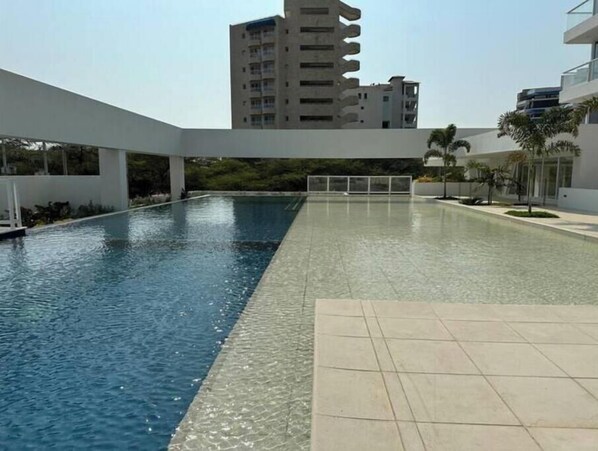 A swimming pool with a tiled deck, surrounded by modern buildings and greenery. - Luxury Loft Porto Horizonte Beach meters away (Magdalena)