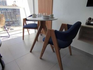 A modern dining area with a round table, two blue chairs, and a view of a cityscape through large windows. - Luxury Loft Porto Horizonte Beach meters away (Magdalena)