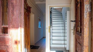 A hallway with a wooden door on the left, a staircase with a metal railing, and a white wall with a framed picture. - Seestern (Rostock)