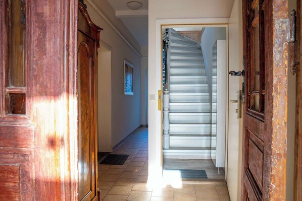 A hallway with a wooden door on the left, a staircase with a metal railing, and a white wall with a framed picture. - Seestern (Rostock)
