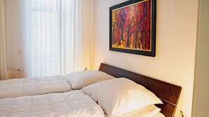 A double bed with white bedding in a room with a wooden headboard, a painting on the wall, and a bedside lamp. - Seestern (Rostock)