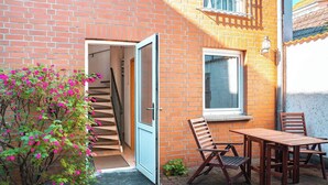 A brick building with a wooden staircase leading to an open door, a window with blinds, and a small outdoor seating area with a table and chairs. - Seestern (Rostock)