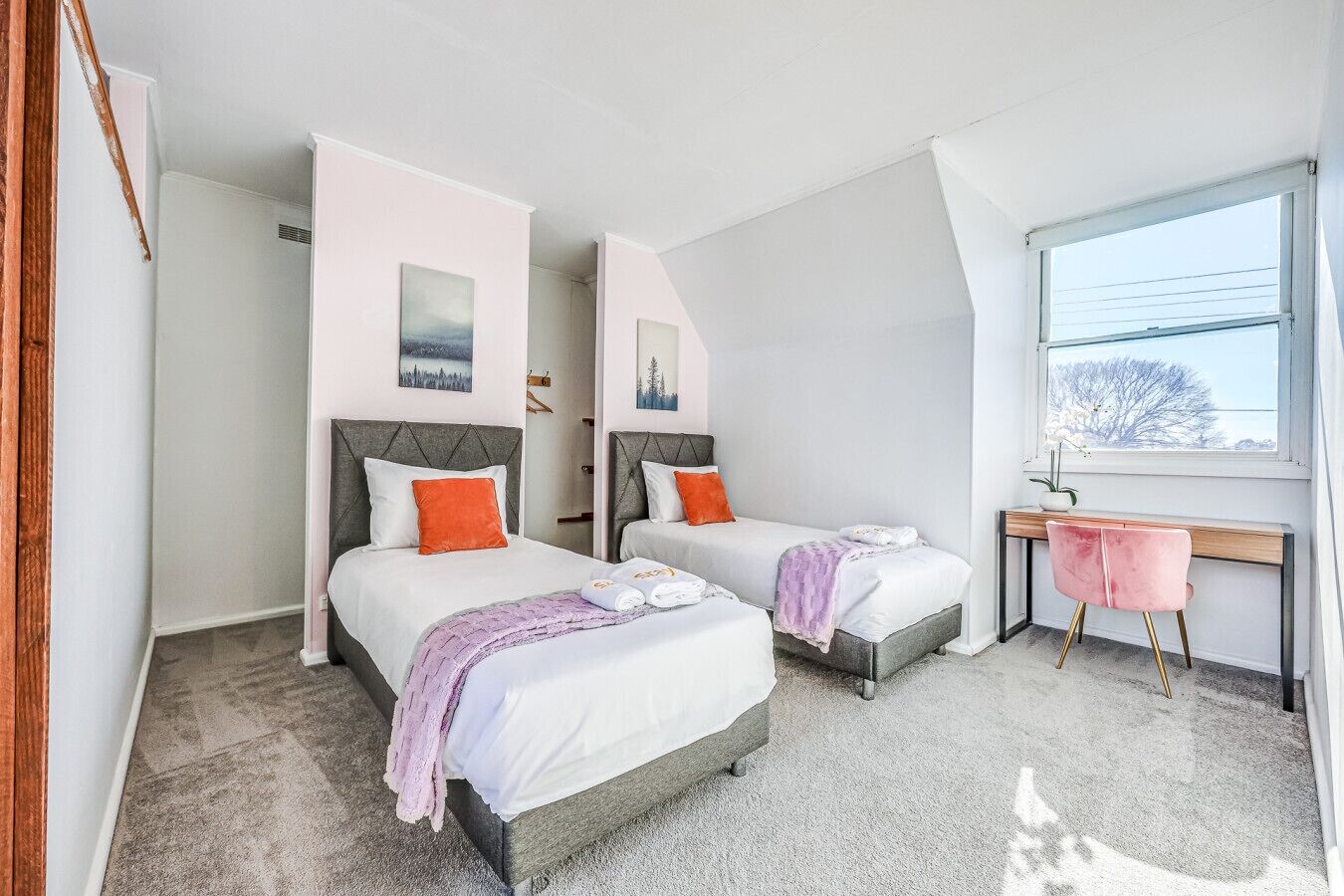 A modern bedroom with two beds, a desk, and a window.