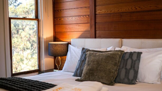 A neatly made bed with white and patterned pillows, a bedside lamp, and a view of trees through a window. - StayAU Private Two-Storey 6 Beds House Wendouree (Wendouree)