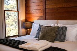 A neatly made bed with white and patterned pillows, a bedside lamp, and a view of trees through a window.