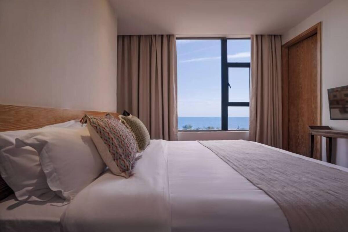 Ein Hotelzimmer mit einem großen Bett, einem Fenster mit Vorhängen und Meerblick.