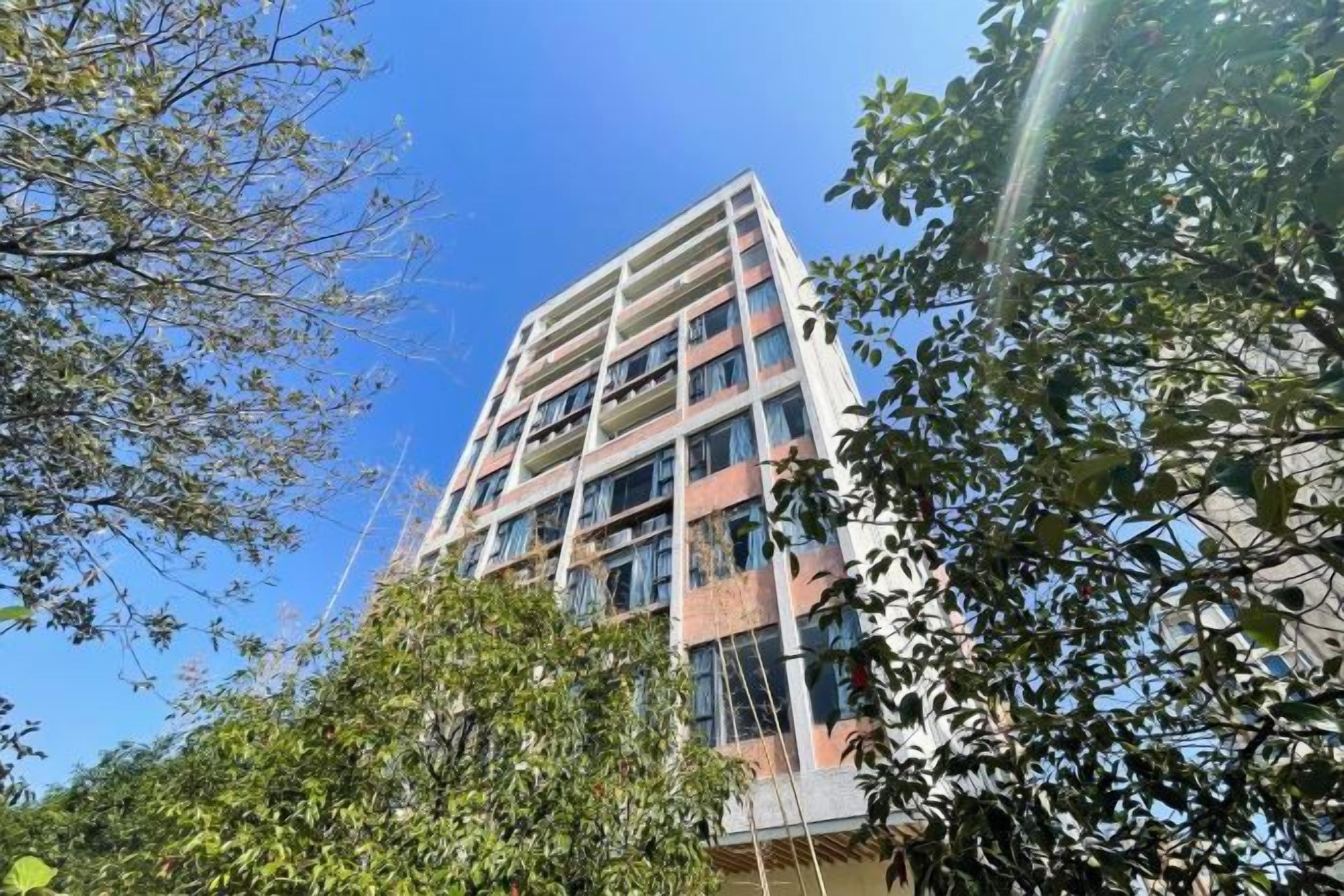 Un immeuble à plusieurs étages, doté de balcons et entouré d’arbres.