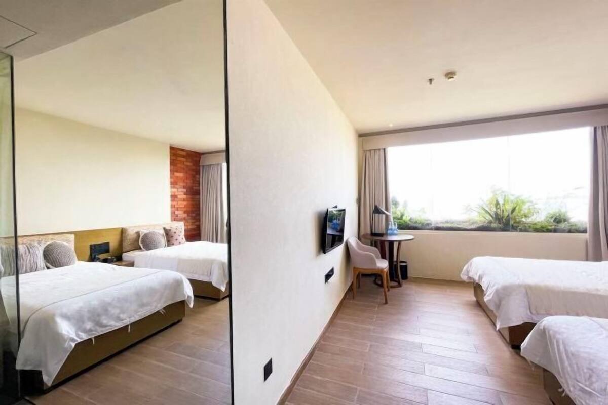 Ein Hotelzimmer mit zwei Betten, einem Fernseher, einem Schreibtisch und einem großen Fenster.