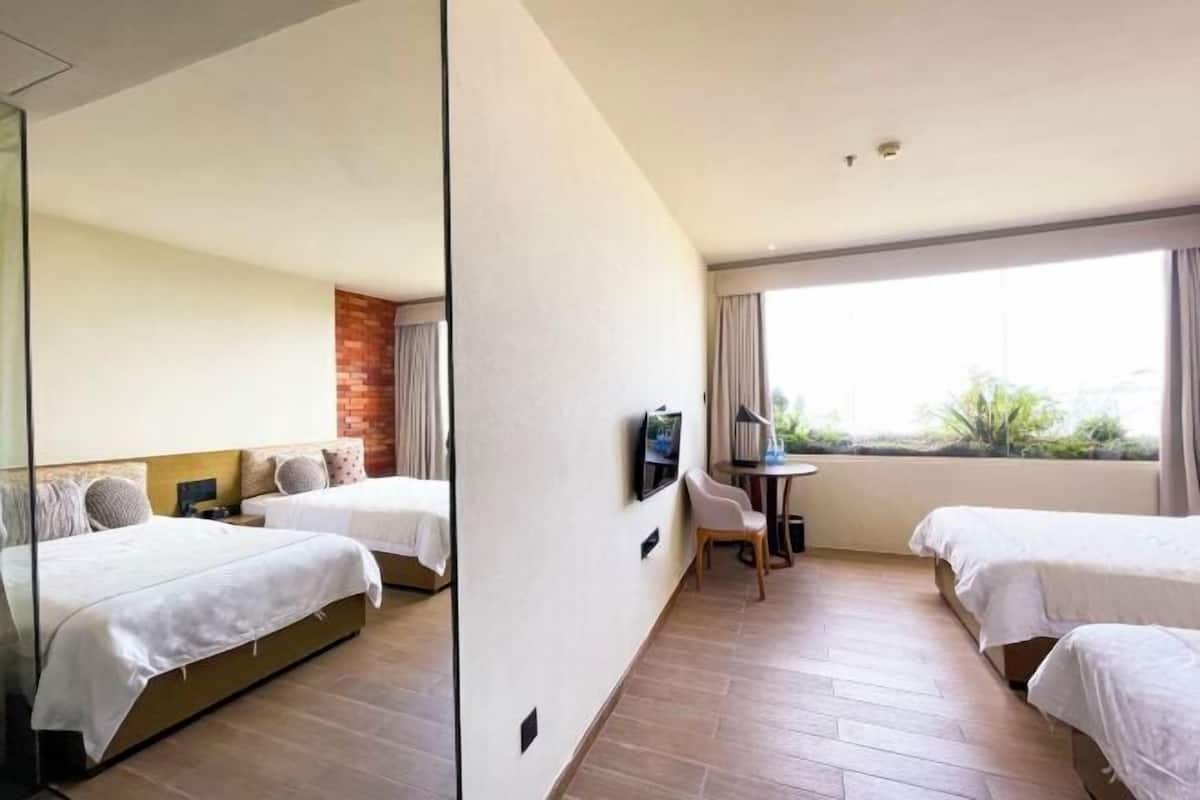 A hotel room with two beds, a TV, a desk, and a large window.