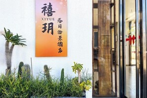 Entrada de un hotel con un letrero en caracteres chinos, puerta de vidrio y una decoración de cinta roja.