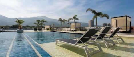 A swimming pool with lounge chairs and palm trees, with mountains in the background.