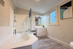 A modern bathroom with a large bathtub, a glass-enclosed shower, and a vanity with a mirror. - StayAU 2BR Home w/ Stunning Views in Tasmania (Trevallyn)