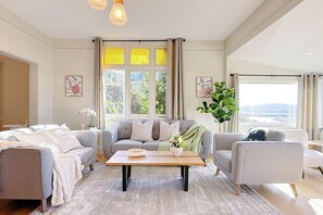 Ein modernes Wohnzimmer mit einer grauen Sofagarnitur, einem Couchtisch und einem großen Fenster mit Vorhängen.