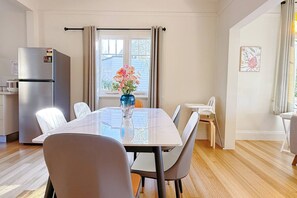 Ein Essbereich mit Tisch, Stühlen, einer Blumenvase, einem Kühlschrank und einem Fenster mit Vorhängen.