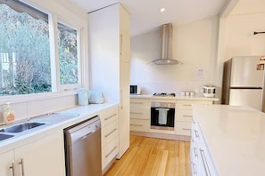 A modern kitchen with a dishwasher, oven, and a window with a view of trees. - StayAU 2BR Home w/ Stunning Views in Tasmania (Trevallyn)