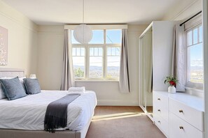 A bedroom with a bed, a dresser, a window with curtains, and a hanging light fixture. - StayAU 2BR Home w/ Stunning Views in Tasmania (Trevallyn)