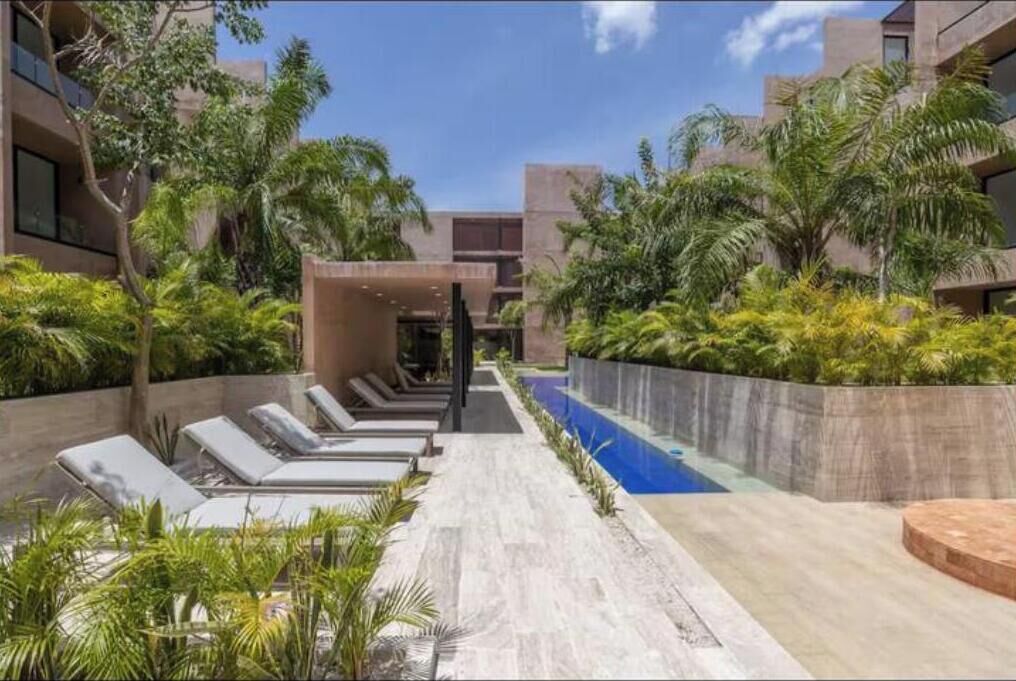 A modern hotel courtyard with a swimming pool, lounge chairs, and tropical landscaping.