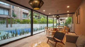 Un interior moderno con comedor, sofá y vistas a una piscina y vegetación exterior.
