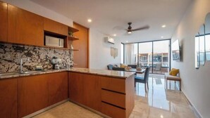 Una cocina moderna con armarios de madera, encimera de mármol y una zona de comedor con separador de vidrio.
