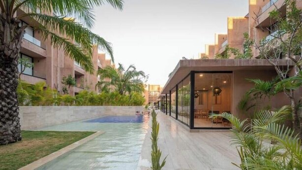 Un edificio moderno con piscina, rodeado de vegetación y palmeras.