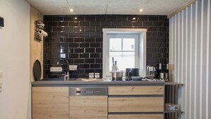 A modern kitchen with black tiled backsplash, wooden cabinets, and a built-in dishwasher. - Lüttjet Huus (Lügde)