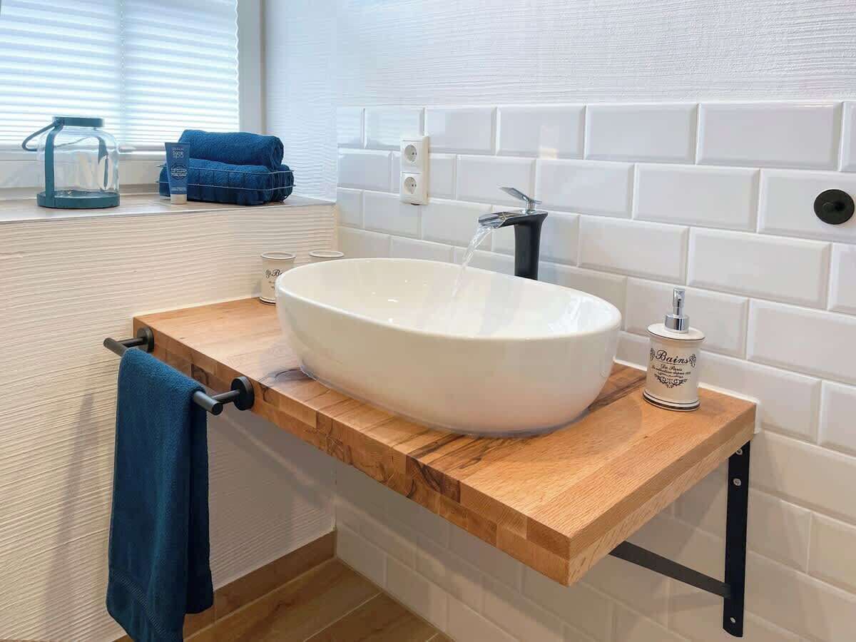 A bathroom with a white vessel sink, a wooden countertop, a blue towel, and a bottle of hand soap.