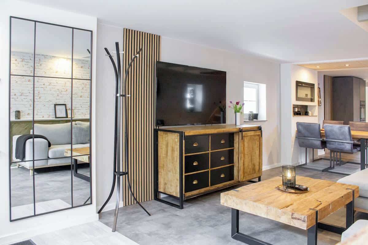 A modern living room with a wooden coffee table, a TV, and a dining area with grey chairs.