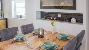 A dining area with a wooden table set for four, a modern kitchen with a built-in stove, and a small window providing natural light. - Lüttjet Huus (Lügde)