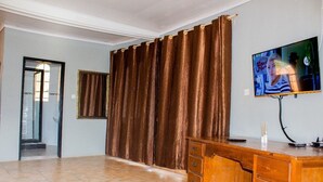 Una habitación con un escritorio de madera, televisor y un amplio ventanal con cortinas.