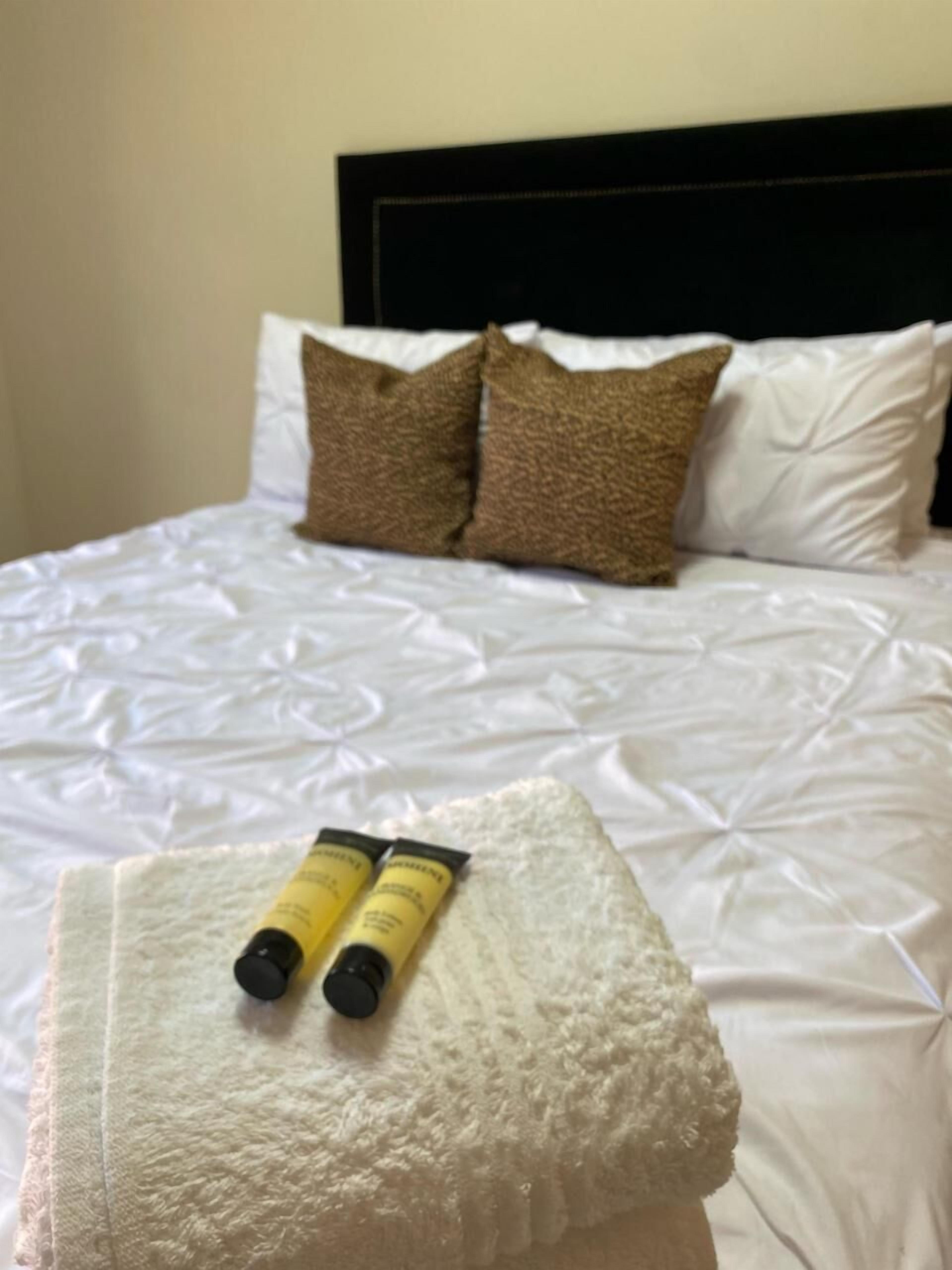 A bed with white bedding and two yellow tubes on a white towel.