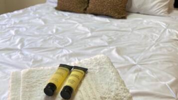 A bed with white bedding and two yellow tubes on a white towel.