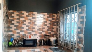 A compact kitchen with a tiled backsplash, a sink, and a window with a metal guard. - StayComidad
Your comfort, Our Priority. (Tamale)
