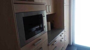 Een keuken met houten kastjes, een inbouwoven en een aanrecht.