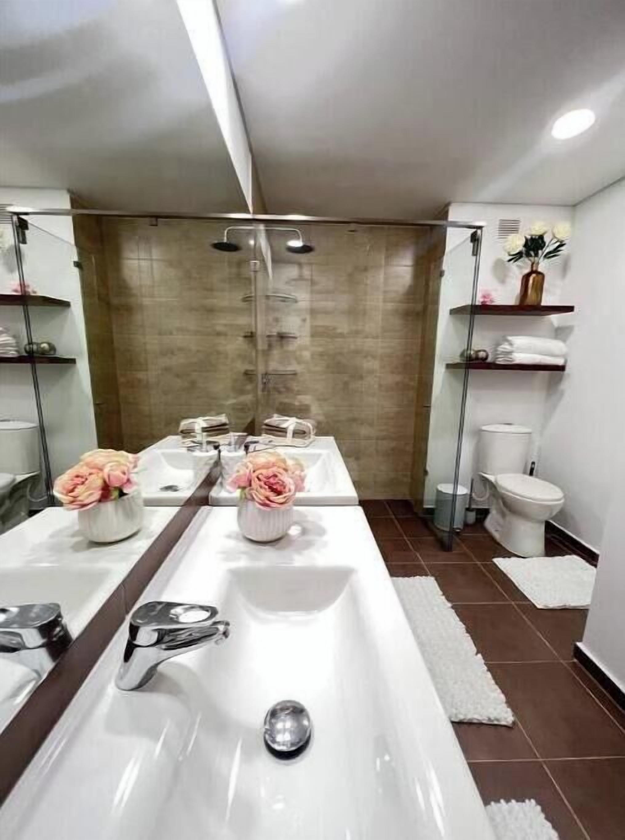 Une salle de bain moderne avec un lavabo central, deux miroirs et un espace douche.