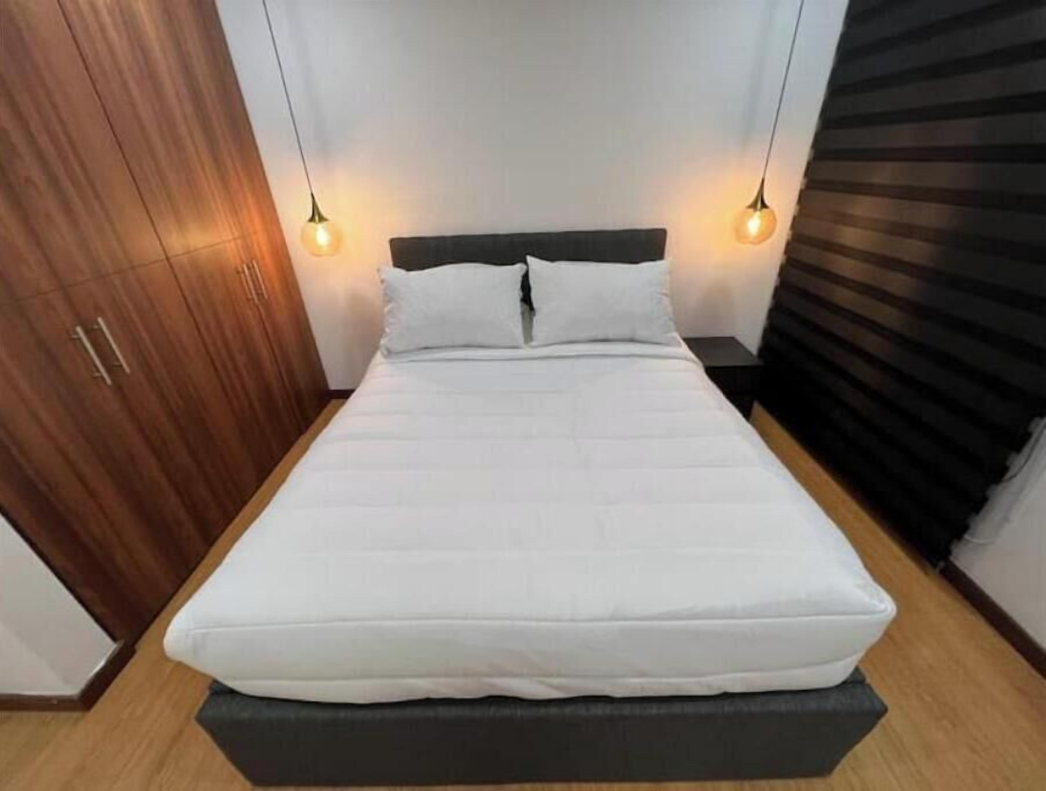 Quarto com cama, guarda-roupa de madeira e duas luminárias pendentes.
