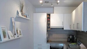 A compact kitchen with white cabinets, a built-in oven, and a coffee maker. - Ferienwohnung Strandperle (Nienhagen)